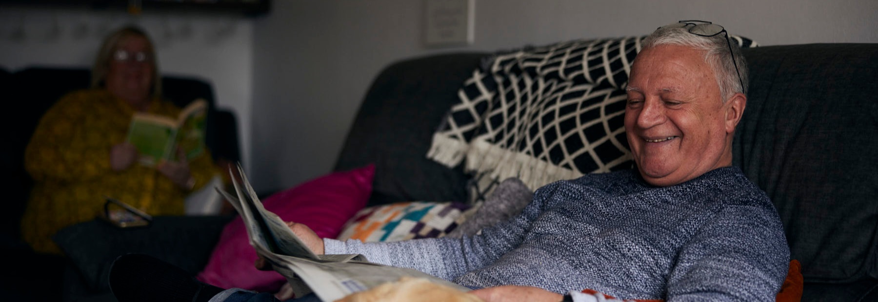 Man sat on sofa smiling reading a newspaper