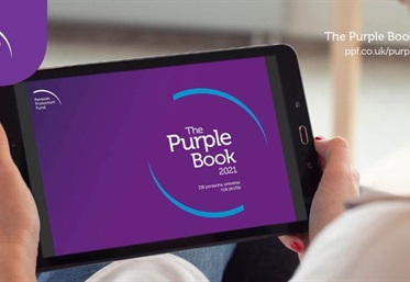 A lady holding a iPad. The iPad screensaver has the text, the purple book displayed on it